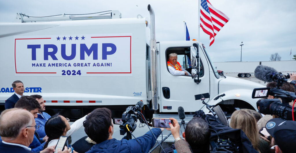 Donald Trump hosts a news conference while seated in a garbage truck with campaign signage on the side
