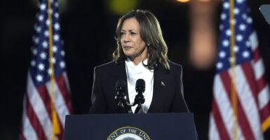 Kamala Harris in a white shirt and a black suit coat in front of American flags