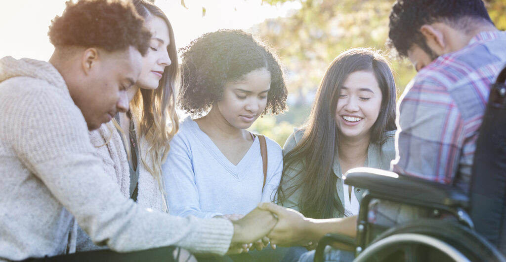 A diverse group of college friends hold hands and pray together on campus.
