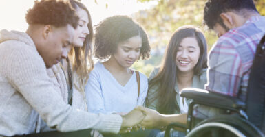 A diverse group of college friends hold hands and pray together on campus.