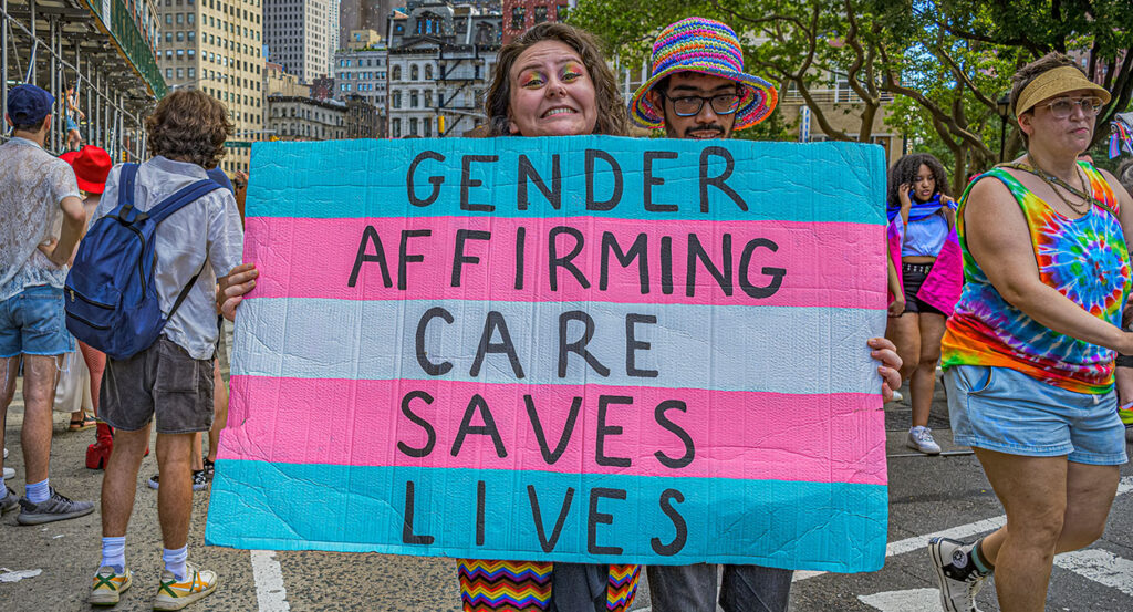 An activist holds a sign reading, "Gender-affirming care saves lives."