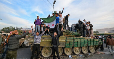 Syrians celebrate while standing on top of a military tank.