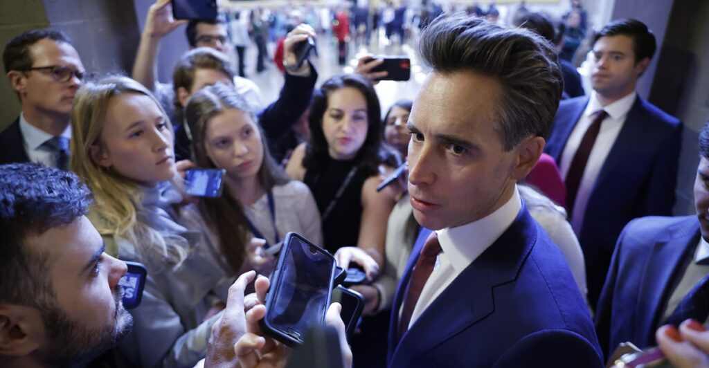 Sen. Josh Hawley stands outside surrounded by a flock of reporters.