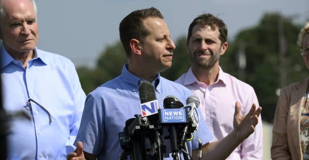 U.S. Representative Jared Moskowitz stands at a podium with microphones and talks to reporters.