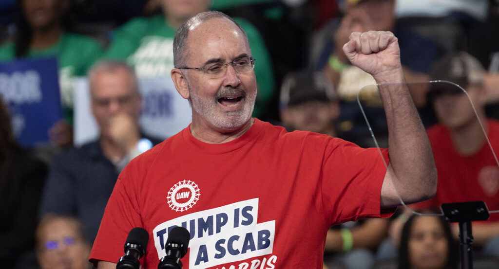 UAW chief Shawn Fain raises his fist while wearing a shirt reading "Trump Is a Scab."