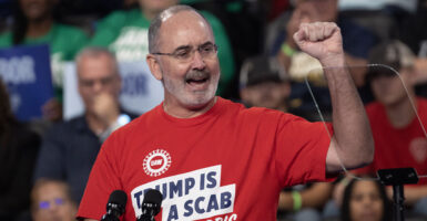 UAW chief Shawn Fain raises his fist while wearing a shirt reading "Trump Is a Scab."