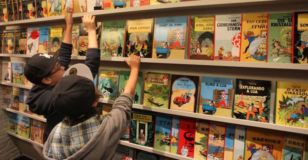 Children reach for the Tintin books on a shelf.