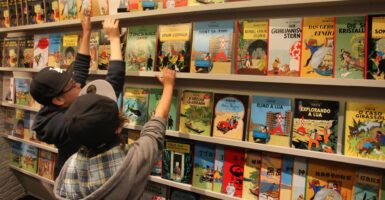 Children reach for the Tintin books on a shelf.