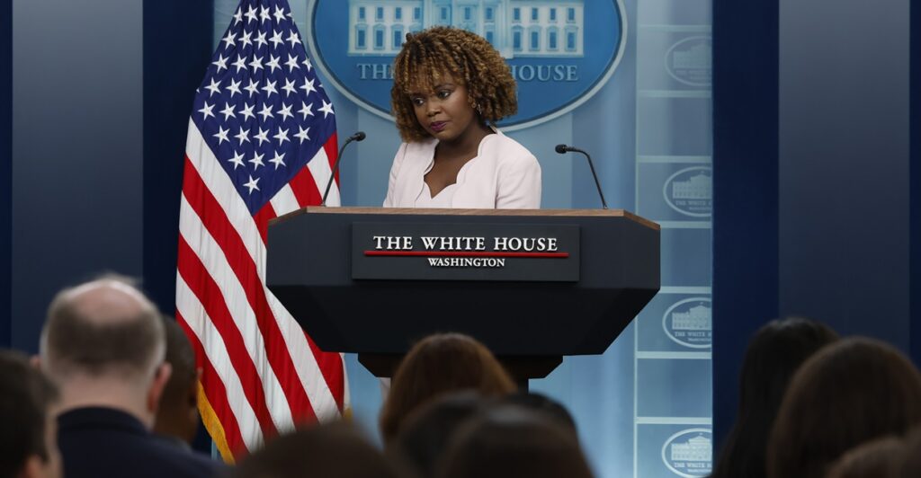 White House press secretary Karine Jean-Pierre speaks during a news conference, standing next to an American flag.