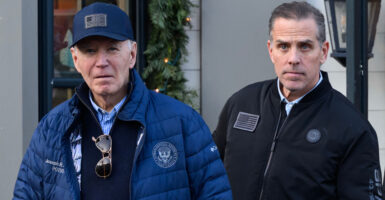 Joe Biden, wearing a navy blue baseball cap and matching winter coat, stands next to his son, Hunter Biden, who is wearing a black zip-up jacket.