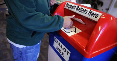 A voter drops a ballot into a ballot box that looks like a Postal Service mailbox