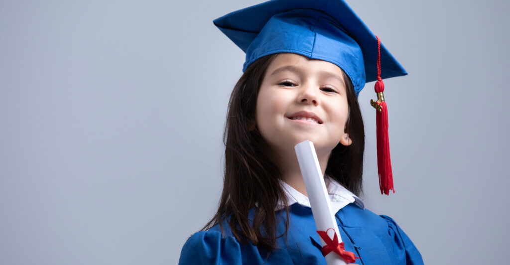 A young girl wearing a blue graduate-style cap and gown and holding a diploma