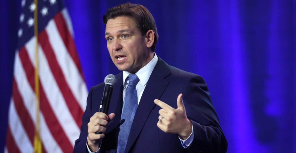 Florida Gov. Ron DeSantis speaking into a hand-held microphone with a U.S. flag as backdrop