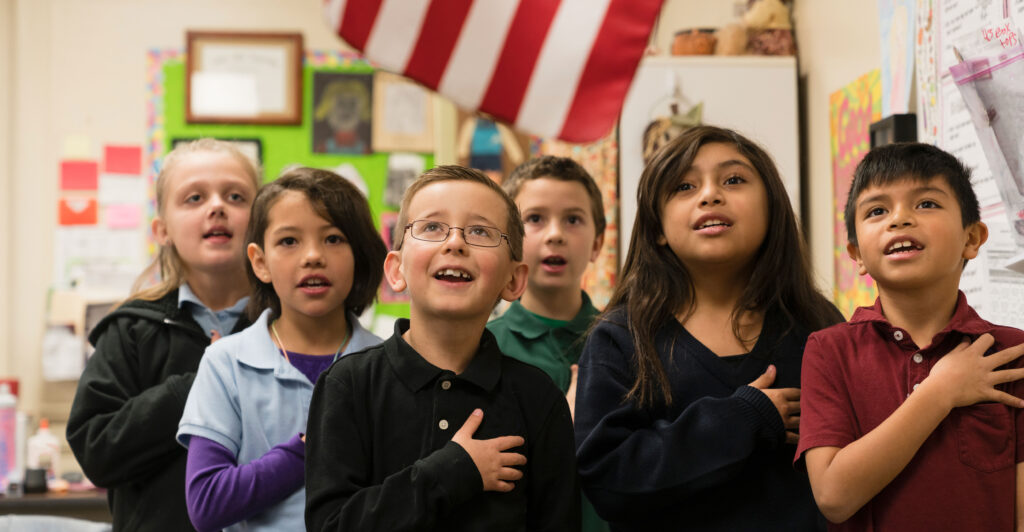 Elementary school-age children pledge allegiance to the American flag.