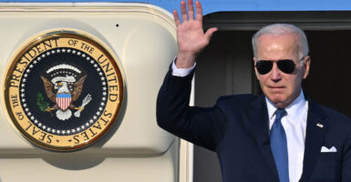 President Joe Biden waves at the door of Air Force One aas he disembarks. The official presidential seal is on the open door beside him.