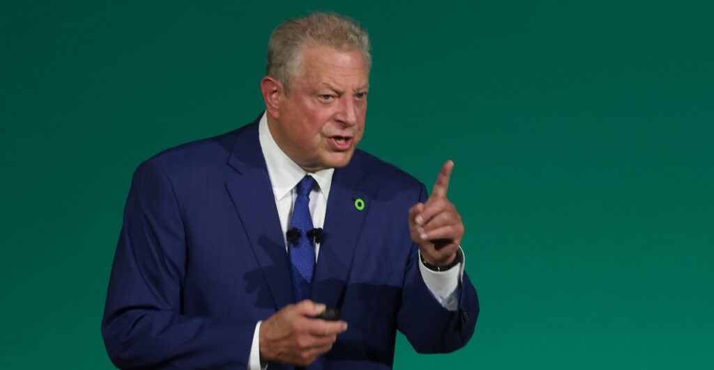 Al Gore holds up his left index finger while talking.