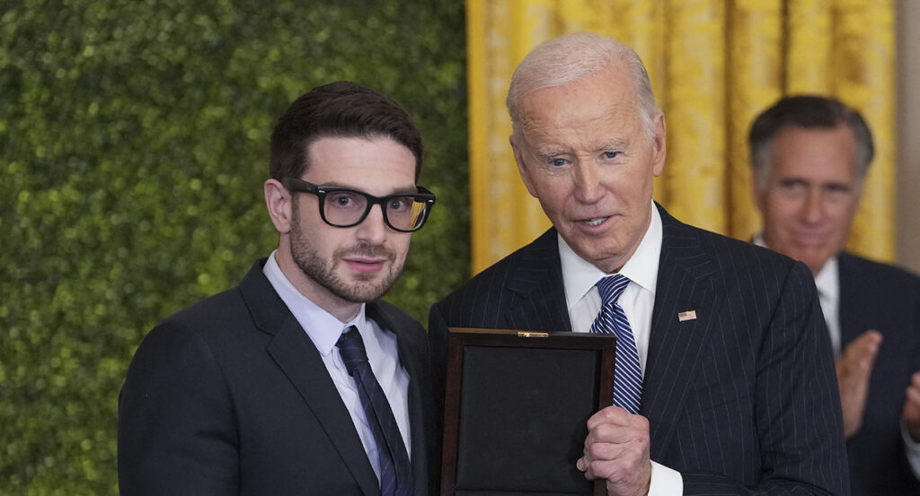 Alex Soros stands next to then-President Joe Biden as Mitt Romney claps in the background