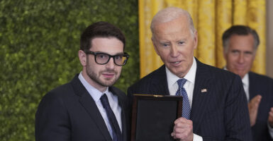 Alex Soros stands next to then-President Joe Biden as Mitt Romney claps in the background