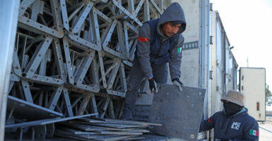 A man in a blue work suit wears a hood as he unloads equipment from a truck.