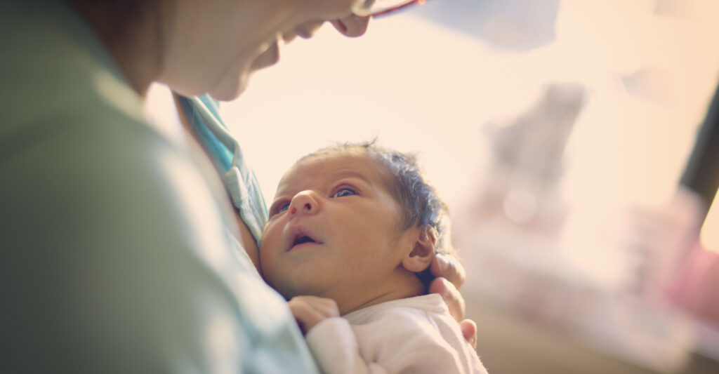 A newborn wearing a white onesie looks up.