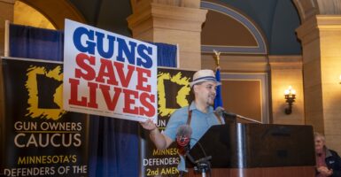 A man wearing a hat holds a sign that states, "Guns Save Lives."