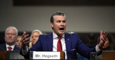 Pete Hegseth raises his arms and talks in an animated fashion during a Senate hearing