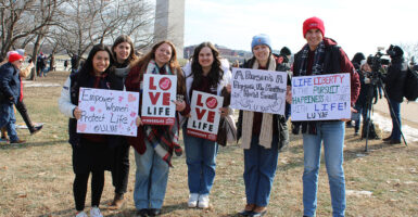Six students hold signs with pro-life messages in front of the Washington Monument.