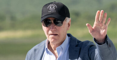 Joe Biden in a blue shirt and a grey sport coat waves in a hat reading "Presidential Retreat Camp David"