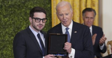 Alex Soros and Joe Biden both hold the Medal of Freedom while they pose for a photo.