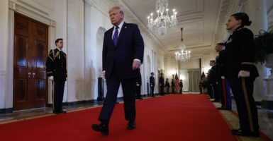 Donald Trump walks with his hands to his side in the White House on a red carpet.