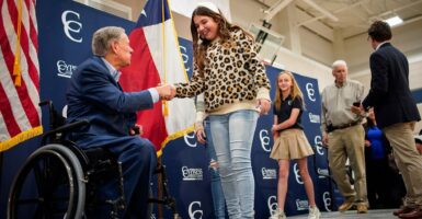 Texas Gov. Greg Abbott is in a wheelchair as he greets a student by shaking her hand.