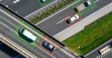 Cars on a highway photographed from the air being tracked electronically with green Or read digital boxes around Each one