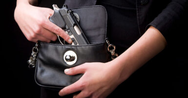 A woman's hands reach into a black purse to pull out a black concealed handgun