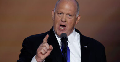 Tom Homan in a dark suit and tie speaking on stage forcefully with his finger pointing forward