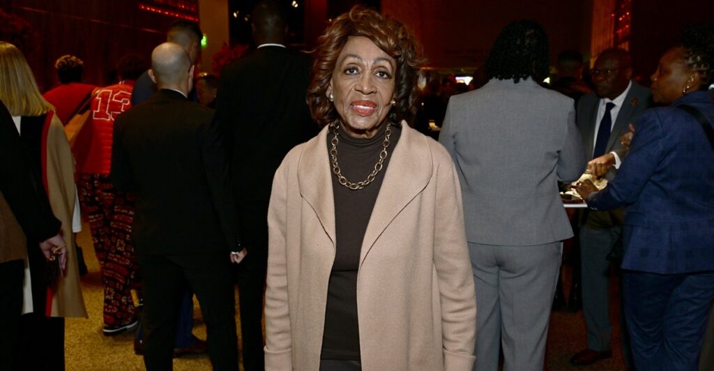 Maxine Waters stands by herself with her hands by her side.
