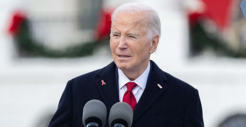 Joe Biden in a dark suit and jacket at a podium on the white house lawn