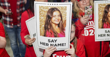 Trump supporters in red Trump 2024 T-shirts hold up signs of a photo of a slain Laken Riley with the caption "say her name!"