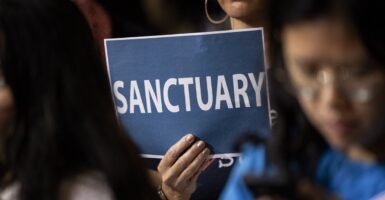 A woman holds up a sign that says "SANCTUARY" at a meeting.