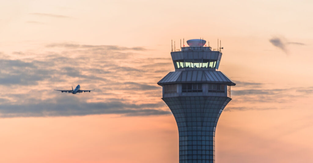 An aircraft approaches an air traffic control tower as it comes in for a landing at sunset.