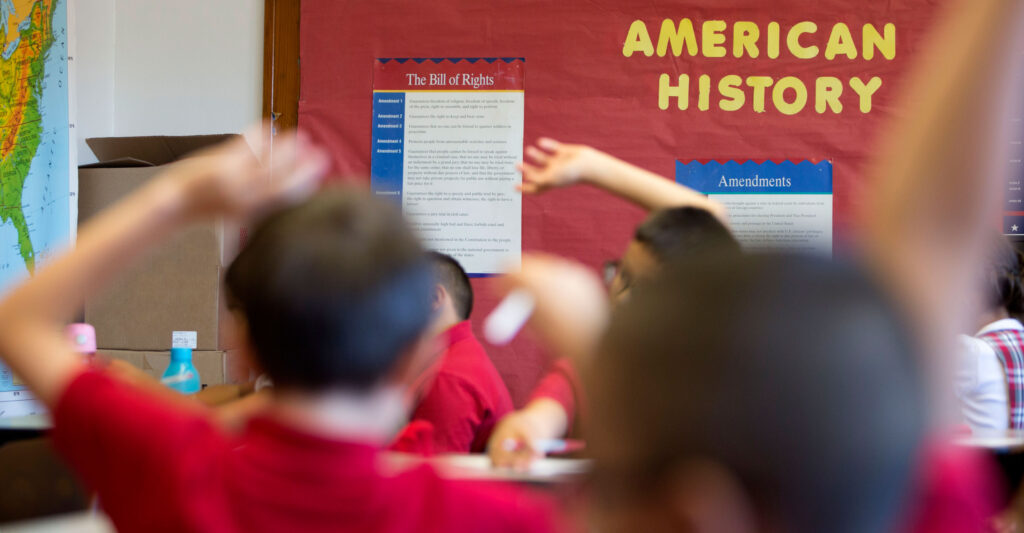 Young students raising their hands to offer to answer a question in an elementary school history class