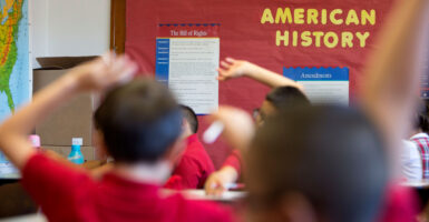 Young students raising their hands to offer to answer a question in an elementary school history class