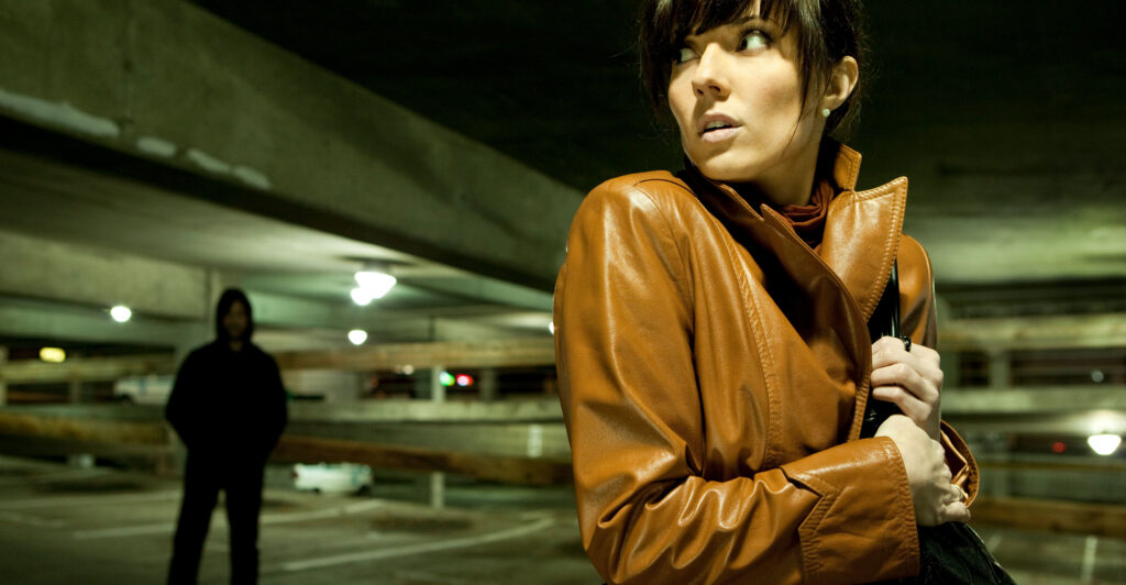 Woman in a parking garage looks over her shoulder nervously at a possible stalker.