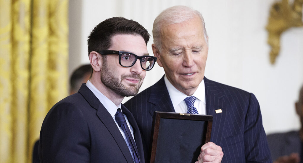 Alex Soros in a suit accepts an award from Joe Biden.