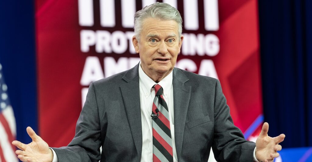 Brad Little stands while his arme are held out.