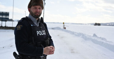 A Royal Canadian mounted police officer standing next to a frozen, snow-covered lake near the U.S. border