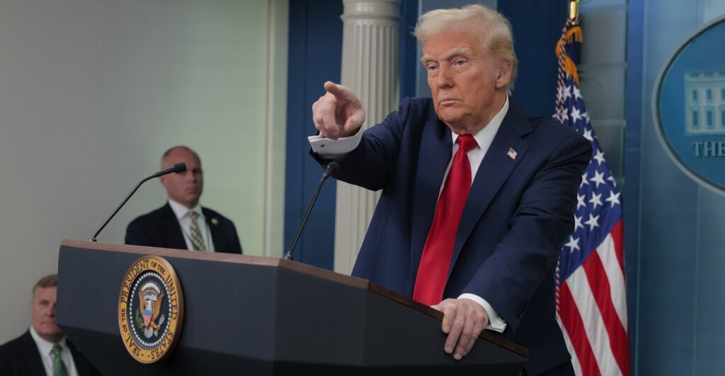 Donald Trump points with his right hand during a press conference while standing at the podium.