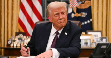 Donald Trump smiles while he signs an executive order
