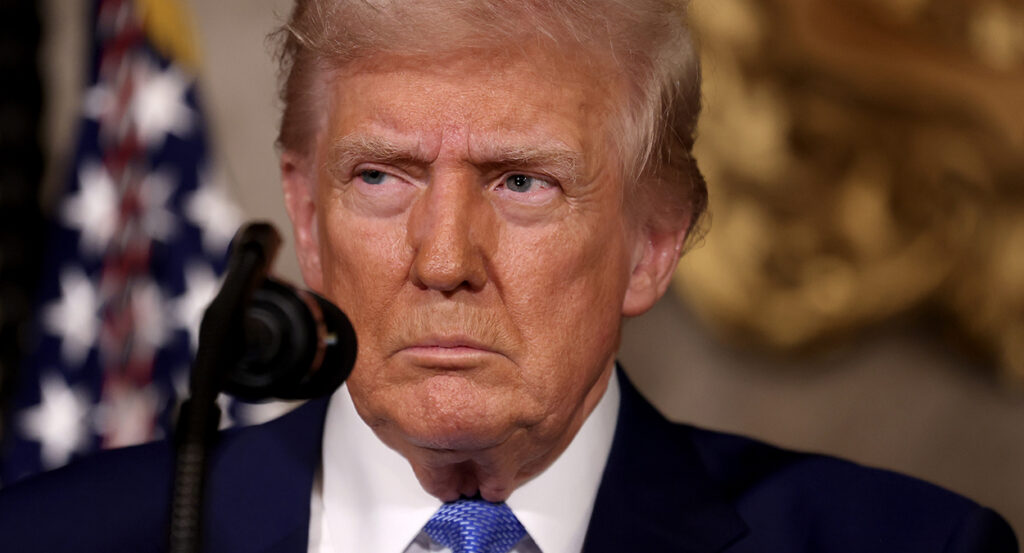 Donald Trump in a blue suit with a blue tie gazes angrily into the distance.