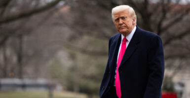 Donald Trump in a blue suit with a red tie walks outside