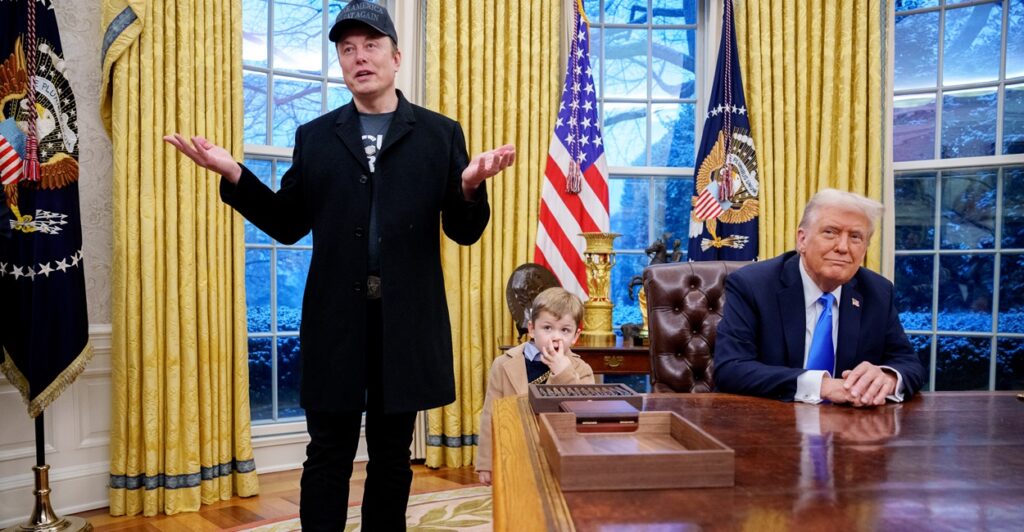 Elon Musk stands in the White House with his hands raised, as if asking a question.